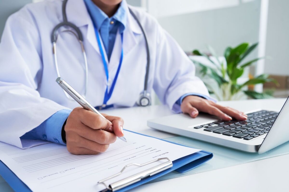 hands-unrecognizable-doctor-writing-form-typing-laptop-keyboard