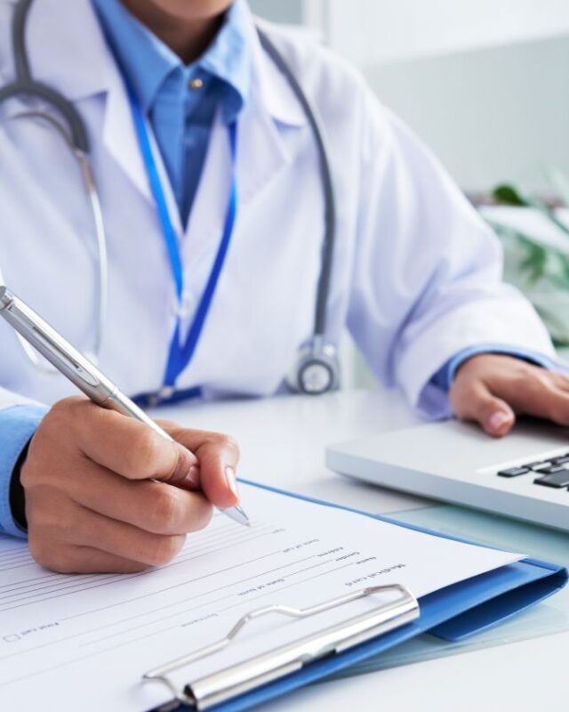 hands-unrecognizable-doctor-writing-form-typing-laptop-keyboard-vertical